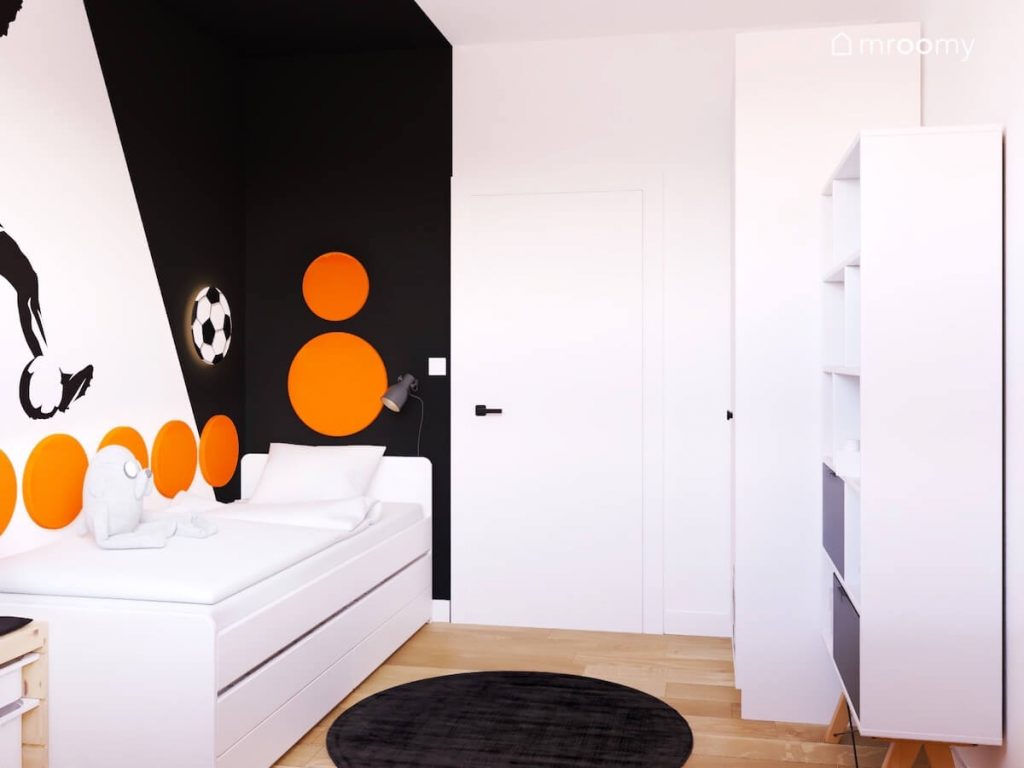 Czarno biały pokój chłopca w wieku szkolnym a w nim białe meble czarny dywanik oraz pomarańczowe panele ścienne