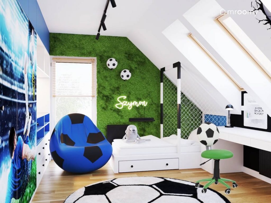 Biały poddaszowy pokój dla chłopca a w nim fototapeta z murawą łóżko w formie bramki fotel i dywan w kształcie piłki
