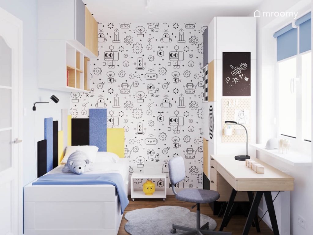 Robotyczna tapeta na ścianie w pokoju chłopca a oprócz tego białe i drewniane meble oraz prostokątne panele ścienne