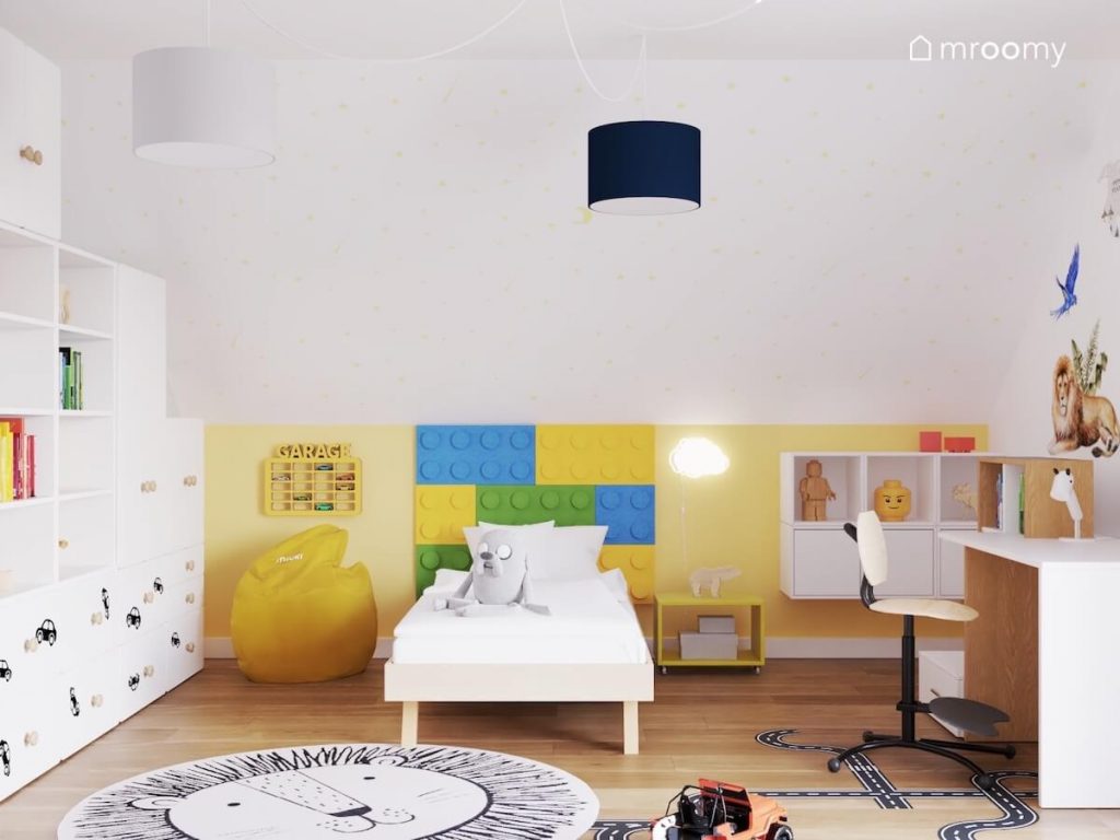 Biało żółty poddaszowy pokój dla chłopca a w nim drewniane łóżko kolorowe panele ścienne żółta pufa oraz skos ozdobiony gwiazdkami