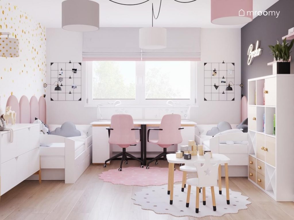 Biało szary pokój dwóch dziewczynek a w nim dwa białe łóżka biało drewniane biurka z różowymi krzesłami organizery ścienne oraz stolik z krzesełkami z oparciami w kształcie korony
