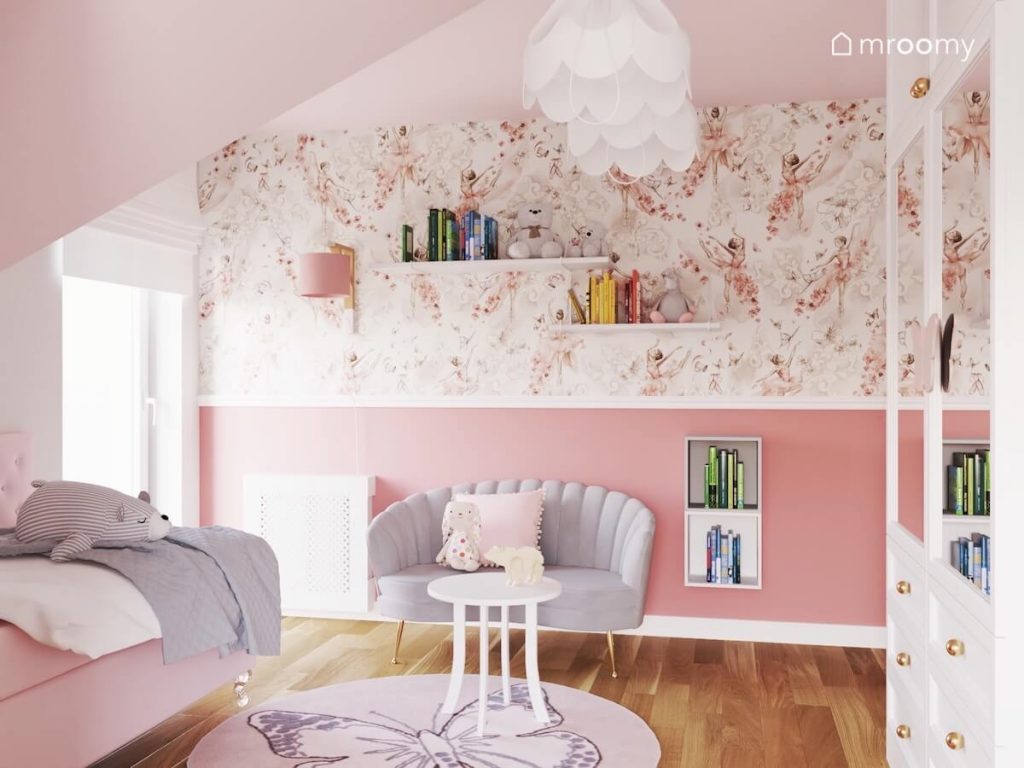 Ściana w pokoju dziewczynki pokryta różową farbą oraz tapetą w baletnice a na niej półki na książki i szara sofa