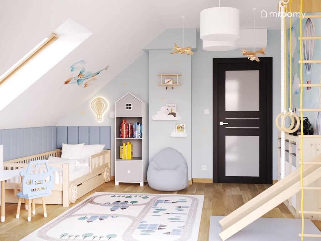 Biało błękitny poddaszowy pokój dla malutkiego chłopca a w nim drewniane łóżko w kształcie wyścigówki regał w kształcie domku dywan z miastem i ozdobne samoloty