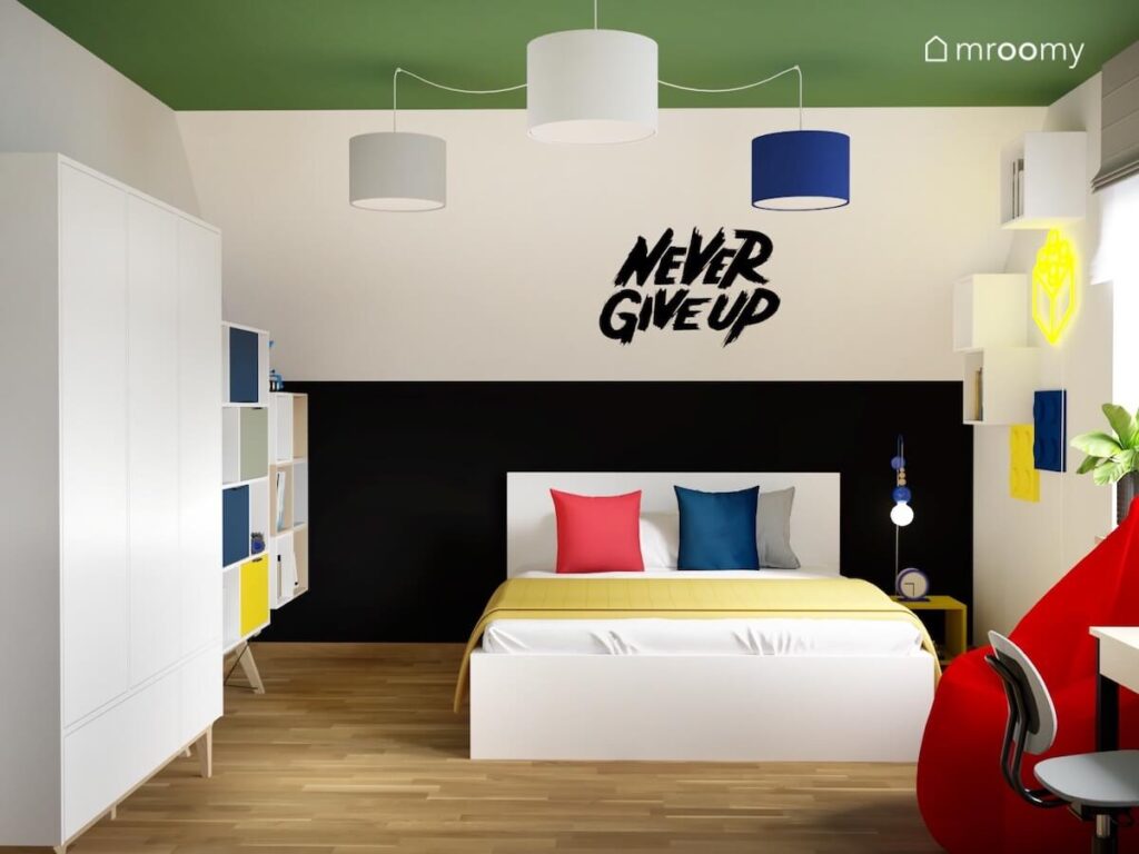 Biały skos i czarna ścianka kolankowa w pokoju dla chłopca a w nim biały meble oraz łóżko z czerwoną i niebieską poduszką i żółtą narzutą
