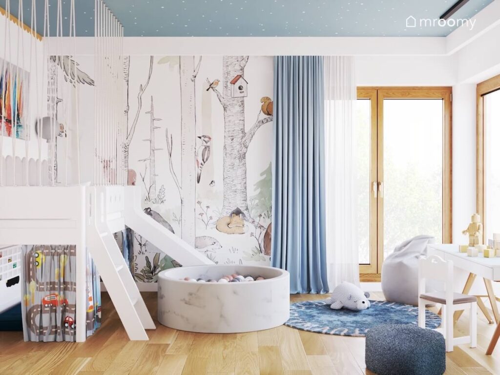 Biała antresola a obok basen z kulkami a na ścianie tapeta z leśnym motywem w pokoju dwóch małych chłopców