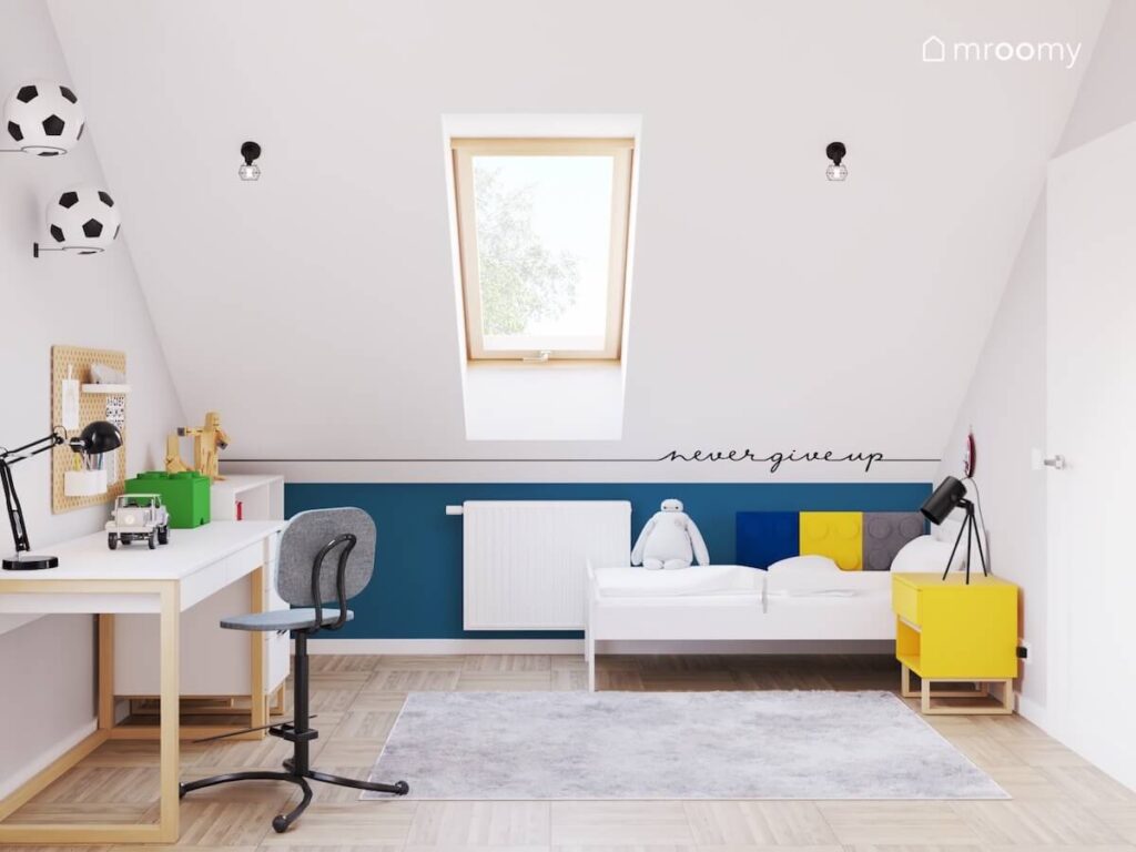 Biało niebieski poddaszowy pokój dla sześciolatka a w nim biurko białe łóżko uzupełnione panelami klockami oraz żółty stolik nocny