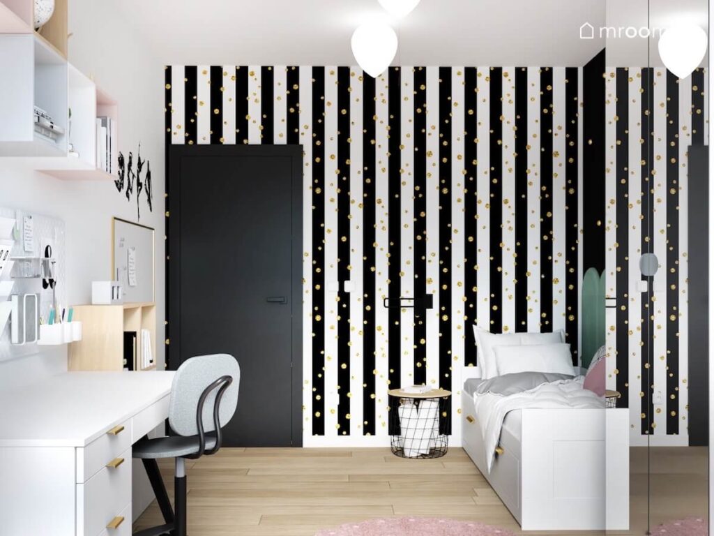 Ściana pokryta tapetą w biało czarne paski i złote kropki a pod nią białe łóżko w pokoju dziewczynki w wieku szkolnym
