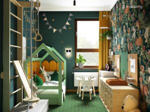 Leśny pokój dla małej dziewczynki a w nim drewniana drabinka gimnastyczna zielone łóżko domek uzupełnione żółtymi panelami ściennymi a także drewniany regał z pojemnikami i stolik z krzesełkiem reniferem
