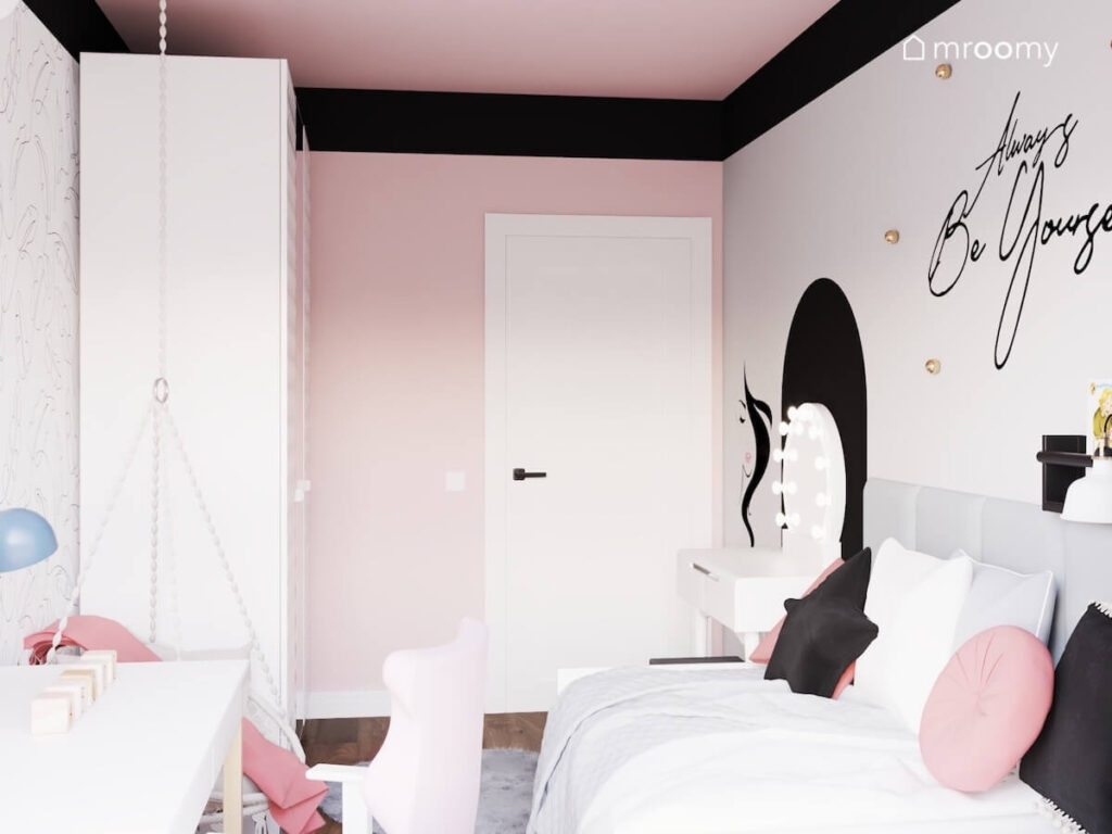 Różowo szary pokój dla dziewczynki a w nim duża biała szafa i toaletka a na ścianie czarne ozdoby oraz złote gałki