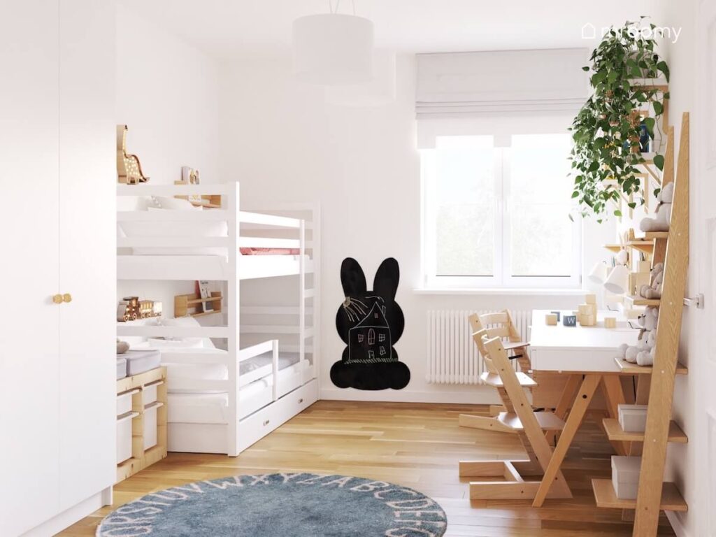 Biały pokój dla siostry i brata a w nim biała szafa białe łóżko piętrowe czarna tablica kredowa w kształcie królika oraz białe biurka na drewnianych nogach