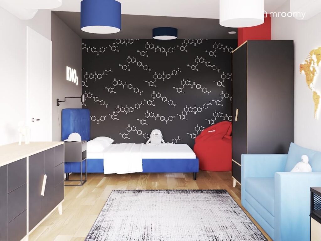 Chemiczna tapeta na jednej ze ścian w biało szarym pokoju nastolatka a także niebieskie tapicerowane łóżko i bordowa pufa