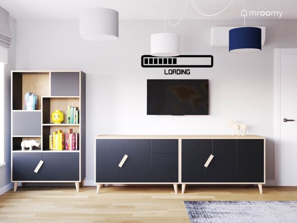 Biało czarny zegar z szafkami a obok dwie komody a nad nimi telewizor i gamingowa naklejka w pokoju nastolatka