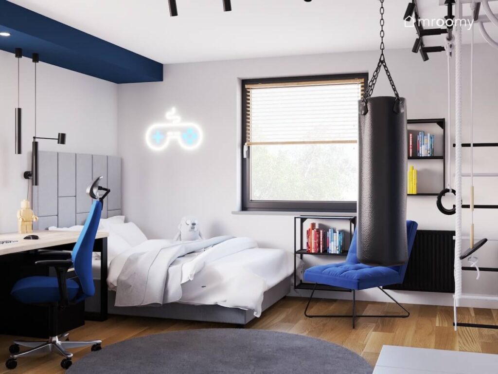 Biało szary pokój dla nastolatka a w nim szare tapicerowane łóżko ledon w kształcie pada worek treningowy i niebieskie krzesła