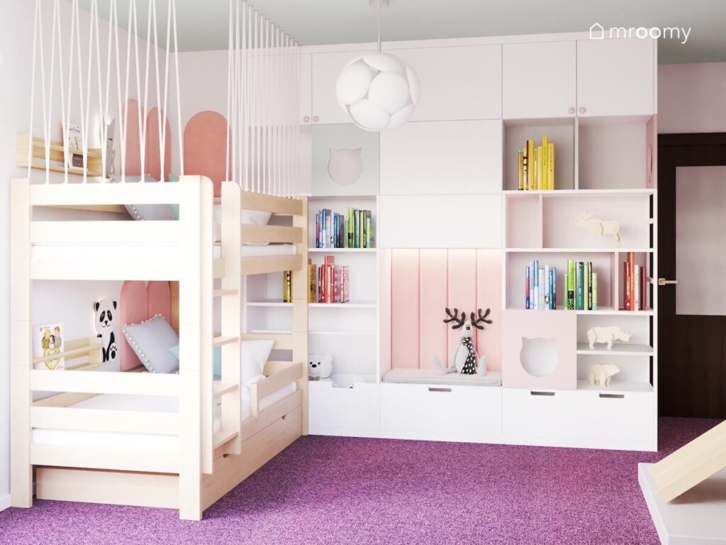 Drewniane łóżko piętrowe w pokoju dziewczynek a obok biała zabudowa meblowa z półkami szafkami siedziskiem oraz kocimi ozdobnikami