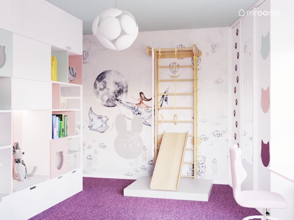 Jasny pokój dla dziewczynek a w nim drewniana drabinka gimnastyczna ze zjeżdżalnią oryginalna lampa a na ścianie kosmiczno podwodna tapeta