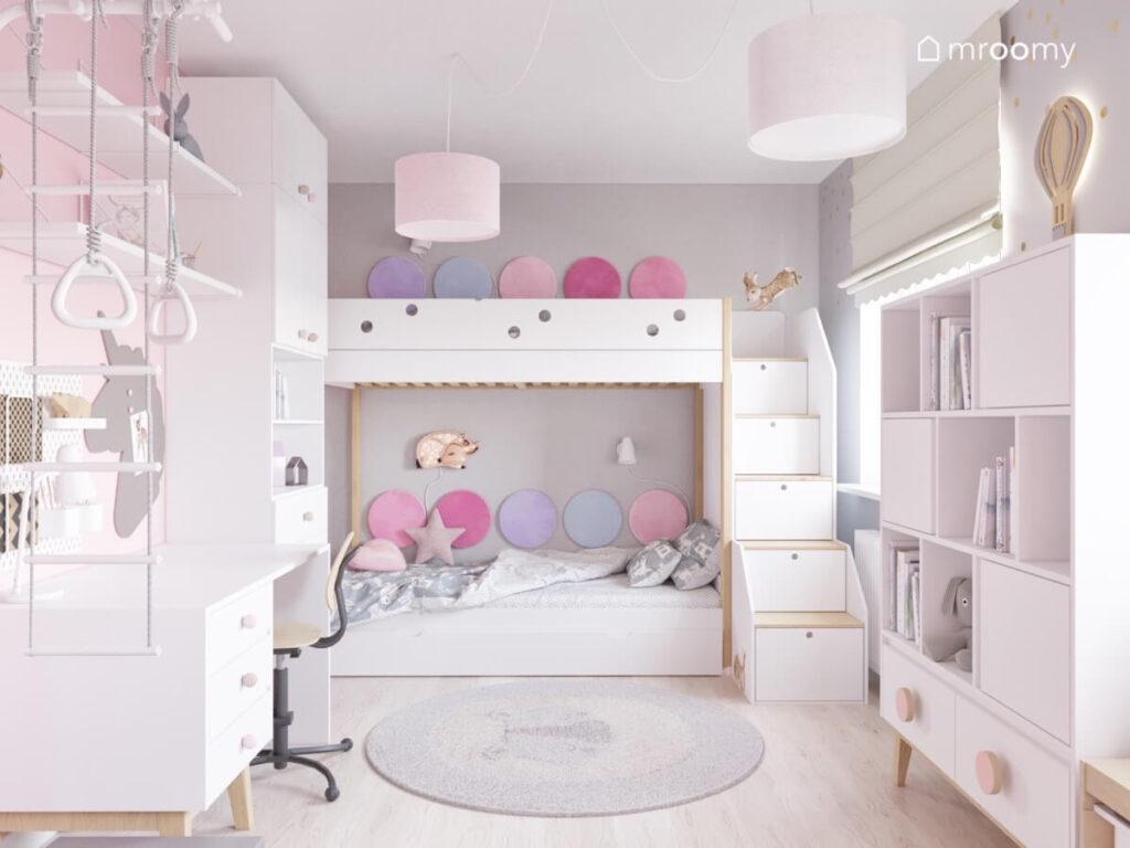 Szaro różowo biały pokój dla dwóch dziewczynek a w nim łóżko piętrowe uzupełnione panelami ściennymi w różnych odcieniach oraz inne białe meble z drewnianymi elementami