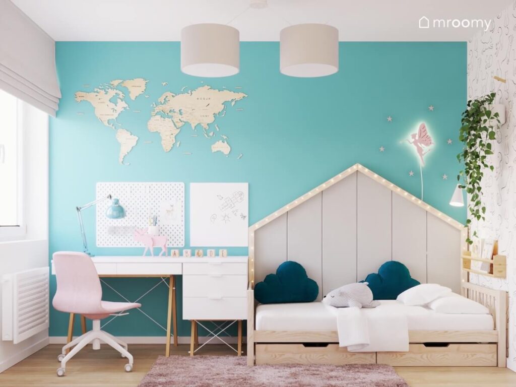 Biało niebieski pokój dla dziewczynki w wieku szkolnym a w nim drewniane łóżko domek uzupełnione lampkami i miękkimi panelami a obok strefa nauki z biurkiem kontenerkiem organizerami i mapą świata