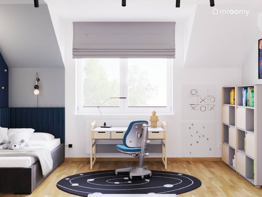 Jasny poddaszowy pokój dla chłopca w wieku szkolnym a w nim ciemne łóżko biało drewniane biurko organizery ścienne oraz kosmiczny dywan