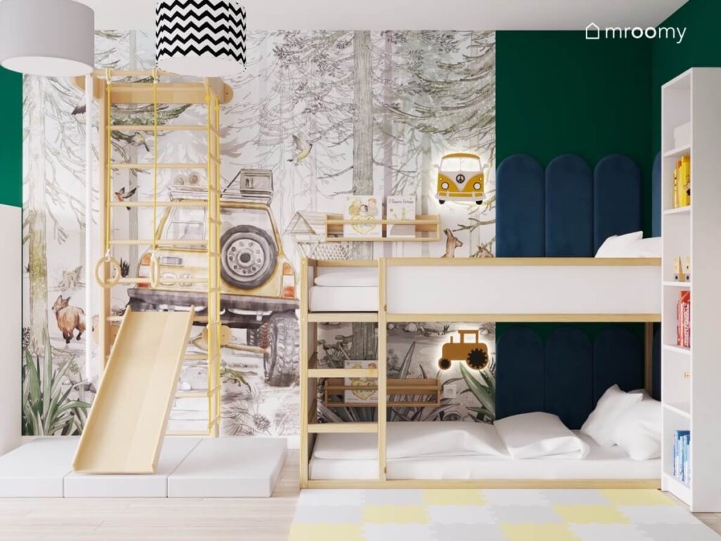 Drewniane łóżko piętrowe uzupełnione granatowymi panelami a obok drewniana drabinka gimnastyczna ze zjeżdżalnią na tle leśnej tapety z samochodem w biało zielonym pokoju dwóch chłopców