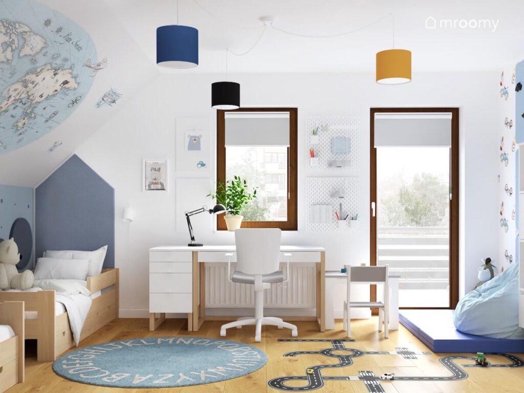 Jasny pokój dla dwóch małych chłopców a w nim drewniane łóżko białe biurko z kontenerkiem a na podłodze dywan z alfabetem i naklejka w kształcie jezdni a u sufitu kolorowe lampy