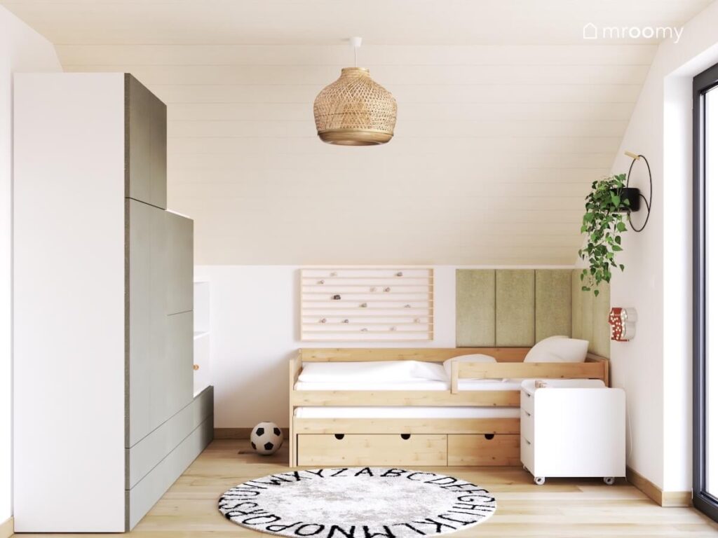 Biało beżowy poddaszowy pokój dla ośmiolatka a w nim drewniane łóżko drewniana półka zielone panele ścienne biało szara szafa i dywan z alfabetem