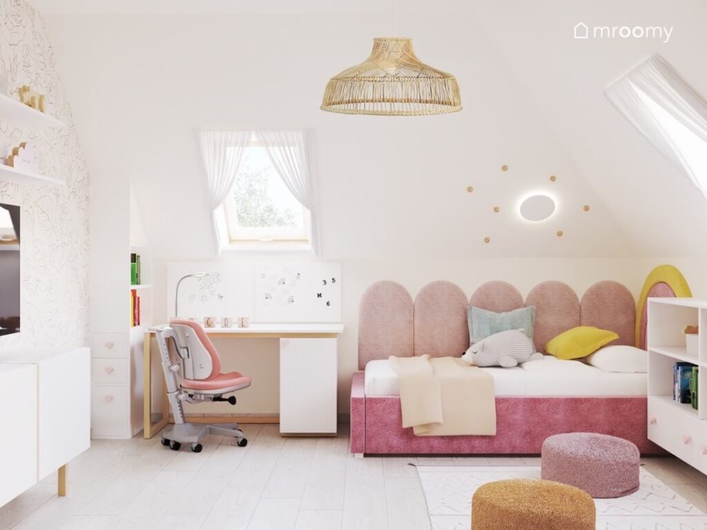 Jasny poddaszowy pokój dla dziewczynki z różowym łóżkiem z miękkimi panelami ściennymi wygodnymi pufami i lampą sufitową z naturalnych materiałów