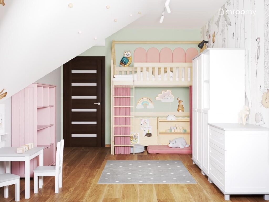 Drewniane łóżko na antresoli w pokoju dwulatki a pod nim miejsce do zabawy zasłonięte różową zasłonką