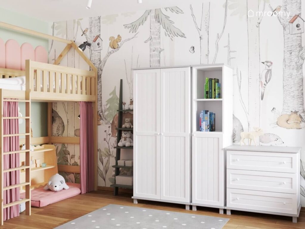 Drewniana antresola białe meble a na ścianie leśna tapeta w pokoju dziewczynki