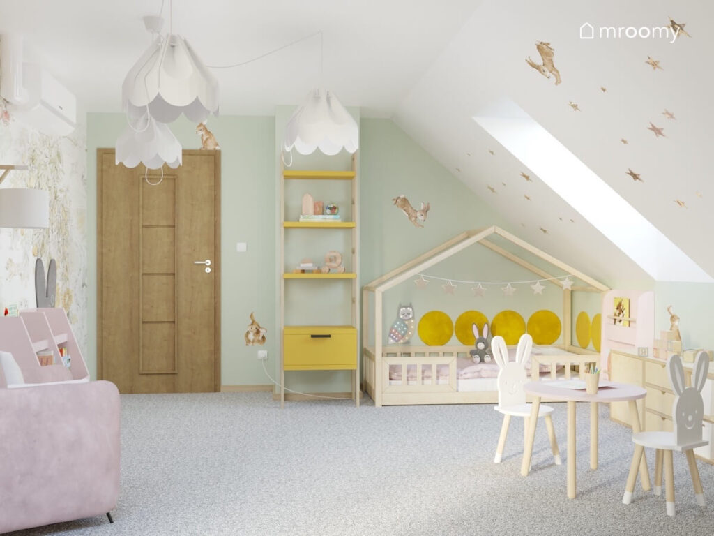 Biało zielony poddaszowy pokój dla dziewczynki a w nim drewniane łóżko domek drewniano żółty regał lampy bezy oraz naklejki króliki