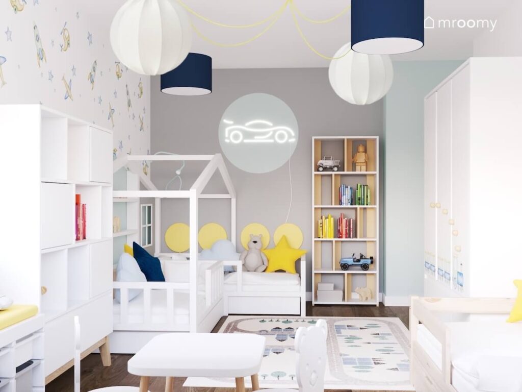 Biało szaro niebieski pokój dla trzech chłopców a w nim białe meble dywan z miastem oraz ledon w kształcie wyścigówki a u sufitu białe i granatowe lampy