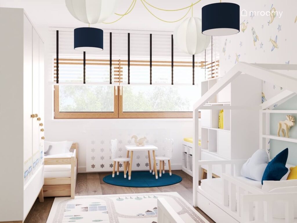 Jasny pokój dla trzech chłopców a w nim biało drewniane meble dywan z miastem oraz niebieski dywan a u sufitu lampy na żółtym zawieszeniu