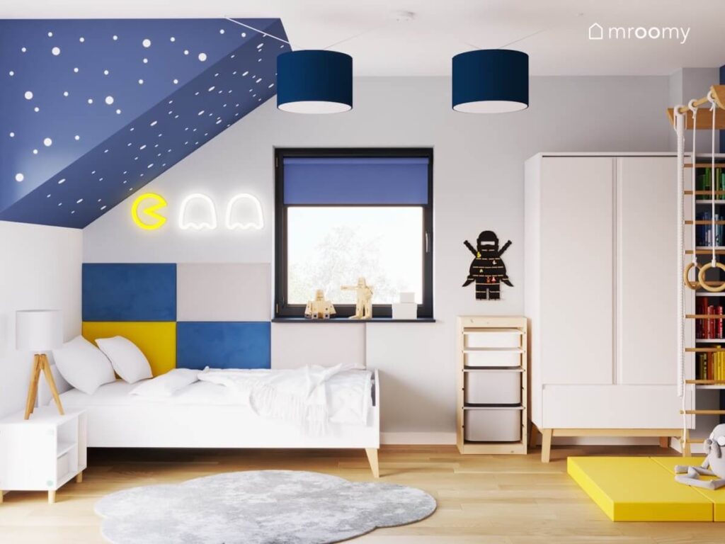 Szaro niebieski pokój dla kilkulatka a w nim białe meble ledon z motywem gry Pacman granatowe lampy i szary dywan chmurka