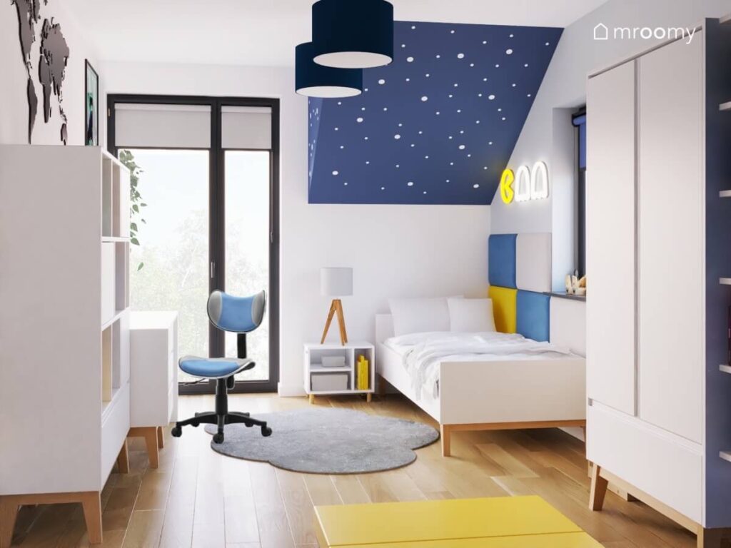 Poddaszowy pokój dla chłopca a w nim białe meble z drewnianymi elementami miękkie panele przy łóżku oraz dywan chmurka