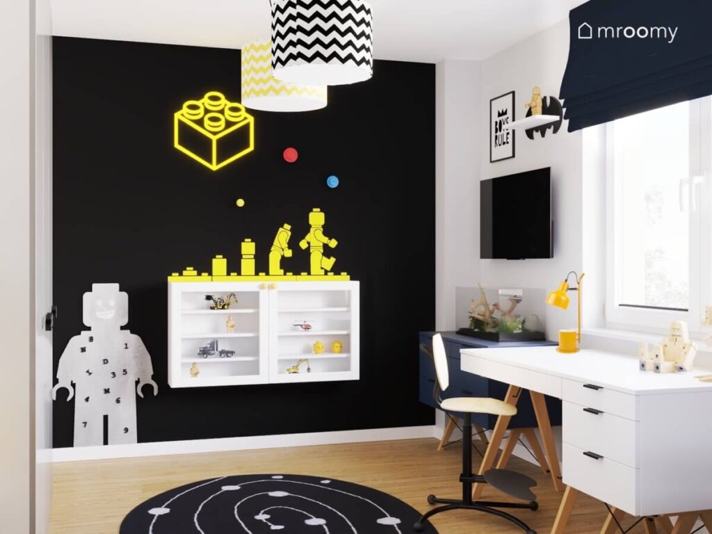 Pomalowana na czarno ściana w pokoju dwóch chłopców a na niej półka na zabawki ledon w kształcie klocka tablica kredowa w kształcie ludzika Lego oraz naklejka z tym samym motywem