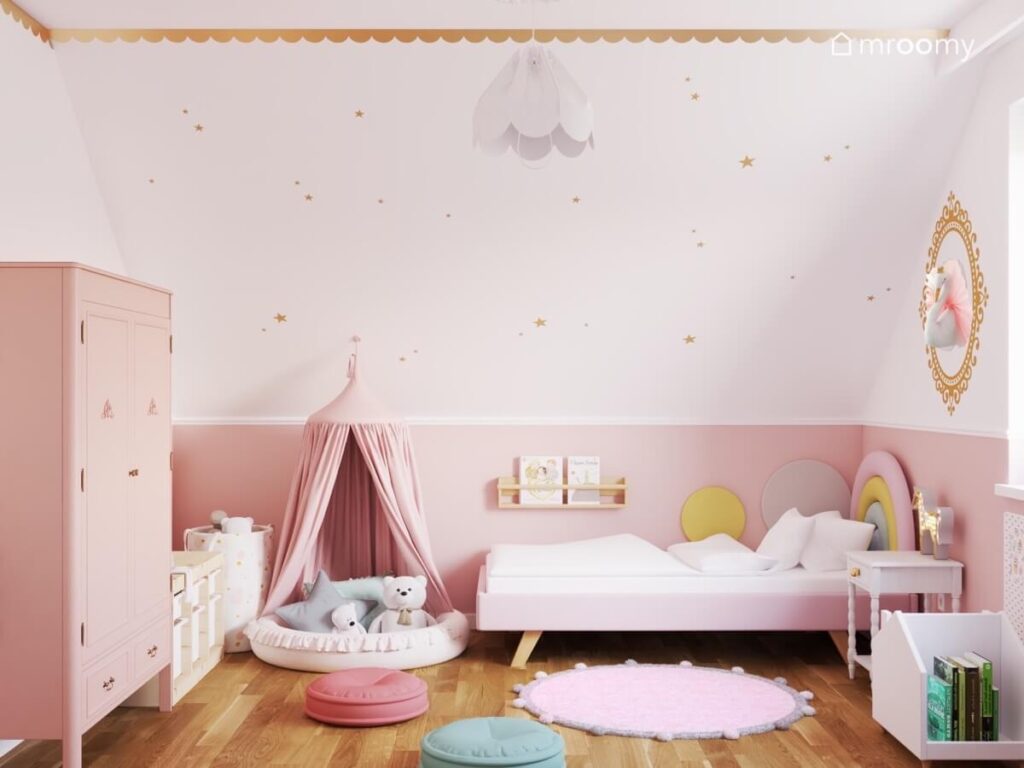 Biały skos w pokoju dziewczynki ozdobiony złotymi gwiazdkami a pod nim różowe łóżko oraz gniazdko osłonięte baldachimem