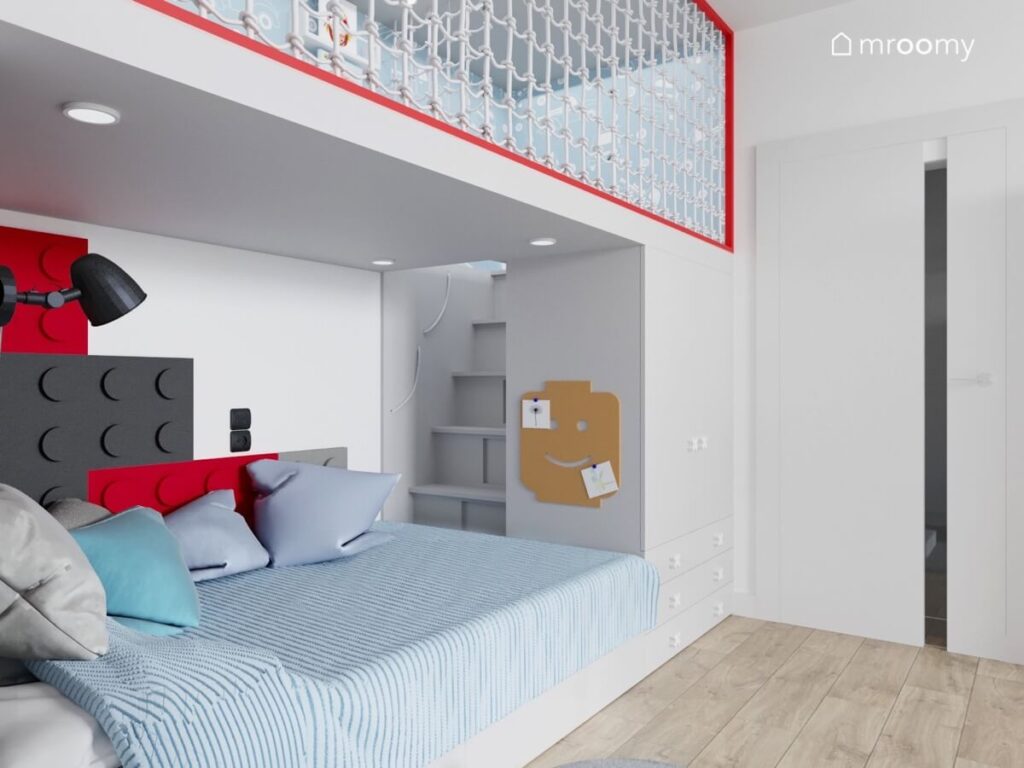 Strefa spania w pokoju małego chłopca a w niej wygodne łóżko panele ścienne w kształcie klocków organizer oraz schodki prowadzące na antresolę