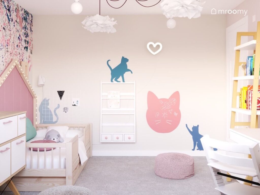 Ściana w pokoju dla małej dziewczynki pokryta kocimi naklejkami a na niej tablica kredowa w kształcie kota biblioteczka oraz ledon w kształcie serca