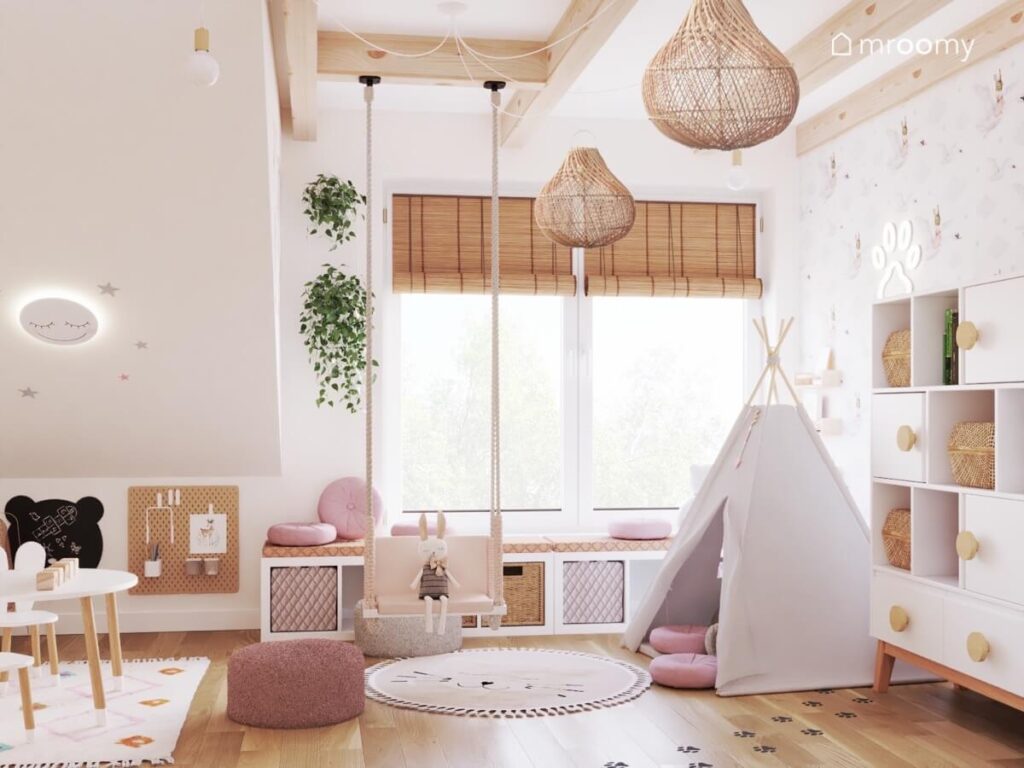 Jasny poddaszowy pokój dwulatki a w nim białe meble drewniane dodatki ozdobne kwietniki oraz namiot tipi i huśtawka