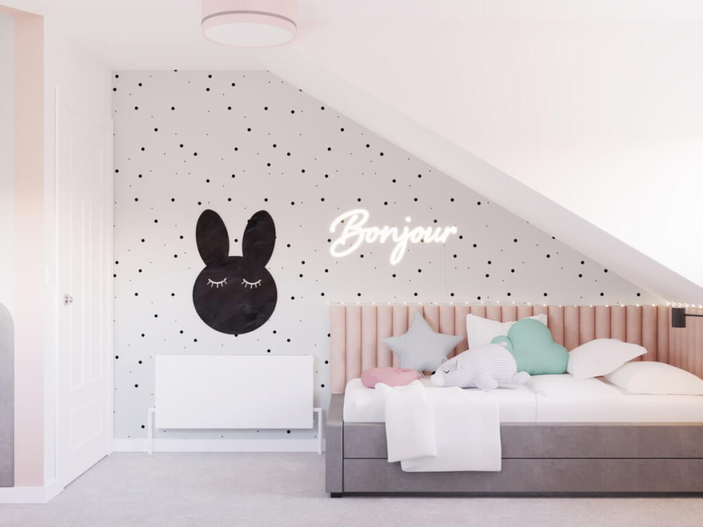 Strefa spania w poddaszowym pokoju dziewczynki w wieku szkolnym a w niej szare łóżko uzupełnione panelami ściennymi ledon w kształcie napisu obok tablica kredowa w kształcie królika a na ścianie tapeta w kropki