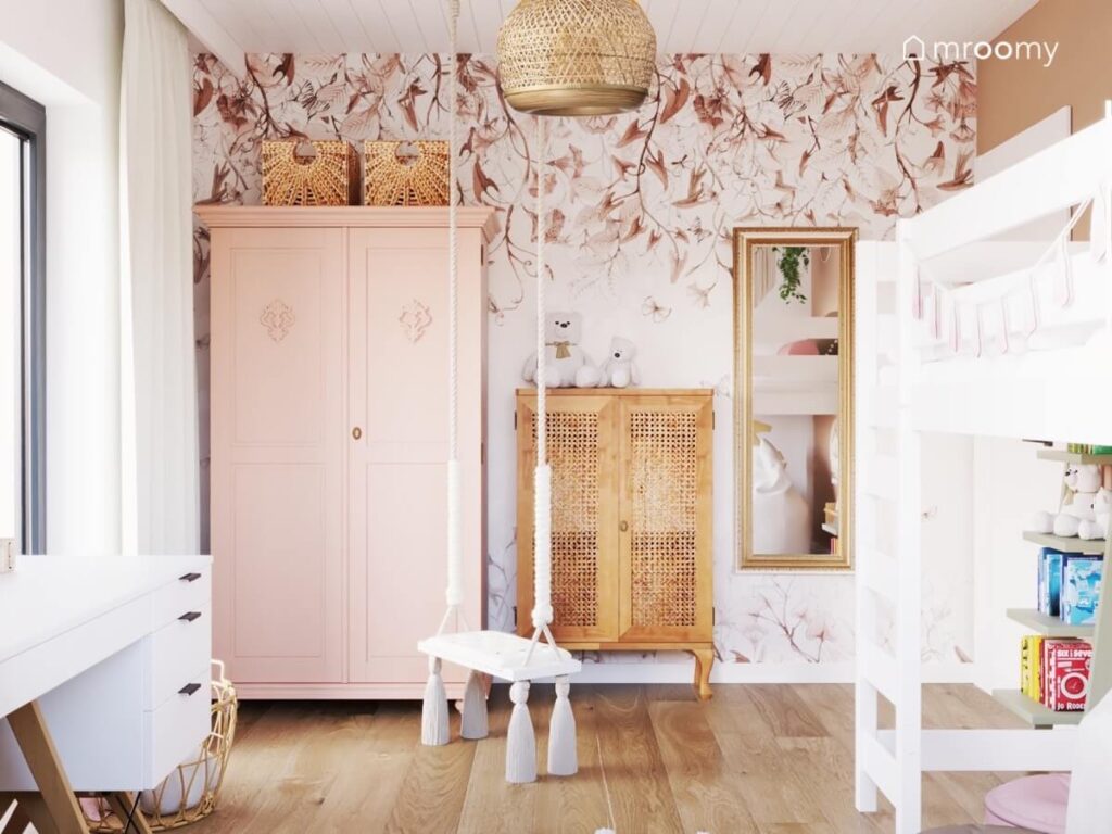 Ściana w pokoju ośmiolatki pokryta tapetą w kwiaty i liście a na niej różowa i drewniana szafa oraz lustro w złotej ramie