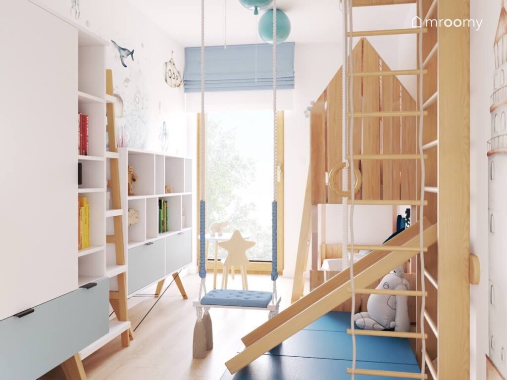 Jasny pokój dla małego chłopca a w nim białe i drewniane meble drabinka gimnastyczna oraz niebieskie dodatki