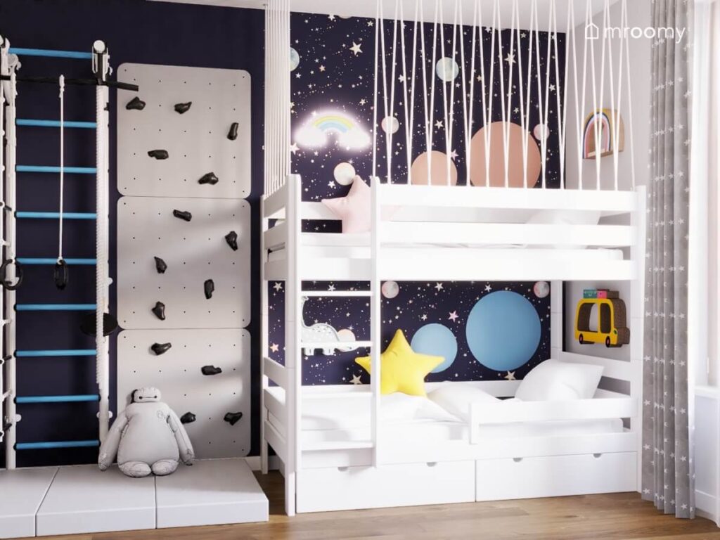 Drabinka gimnastyczna ścianka wspinaczkowa oraz łóżko piętrowe uzupełnione miękkimi panelami półeczkami na książki i lampkami nocnymi w granatowo szarym pokoju rodzeństwa