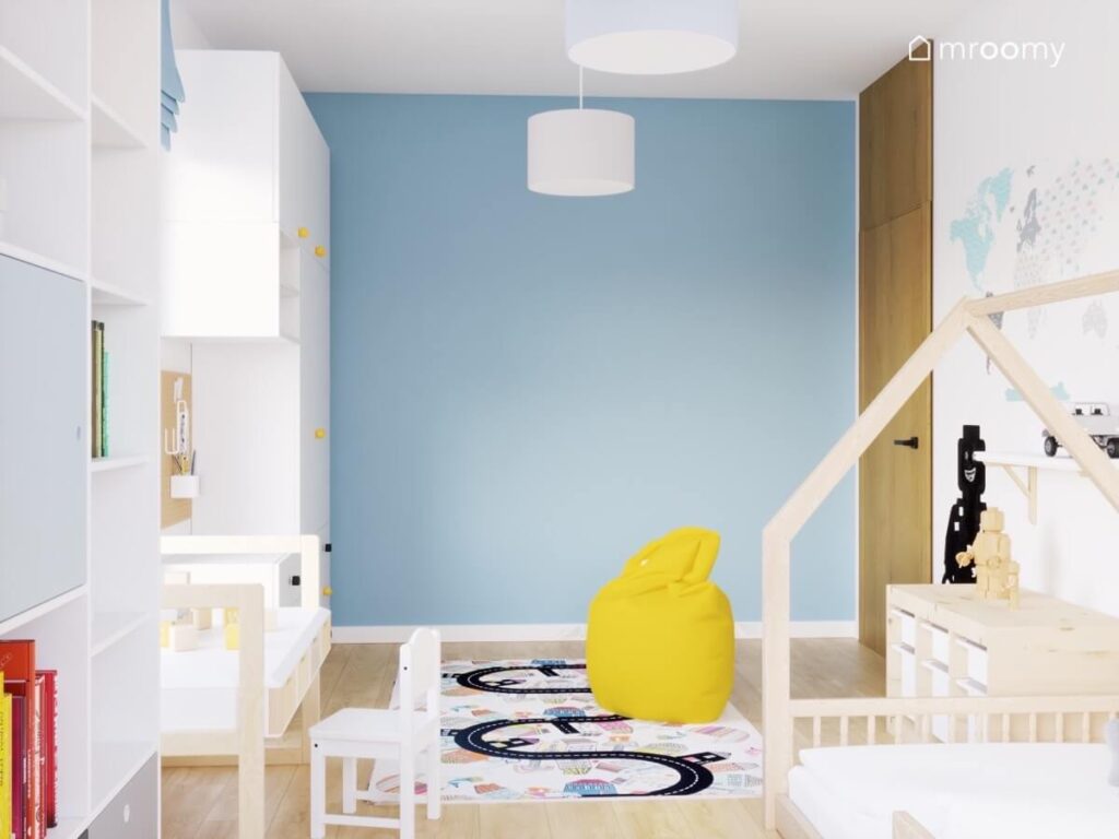 Niebiesko biały pokój trzylatka a w nim białe meble żółta pufa dywan z miastem oraz drewniane łóżko domek
