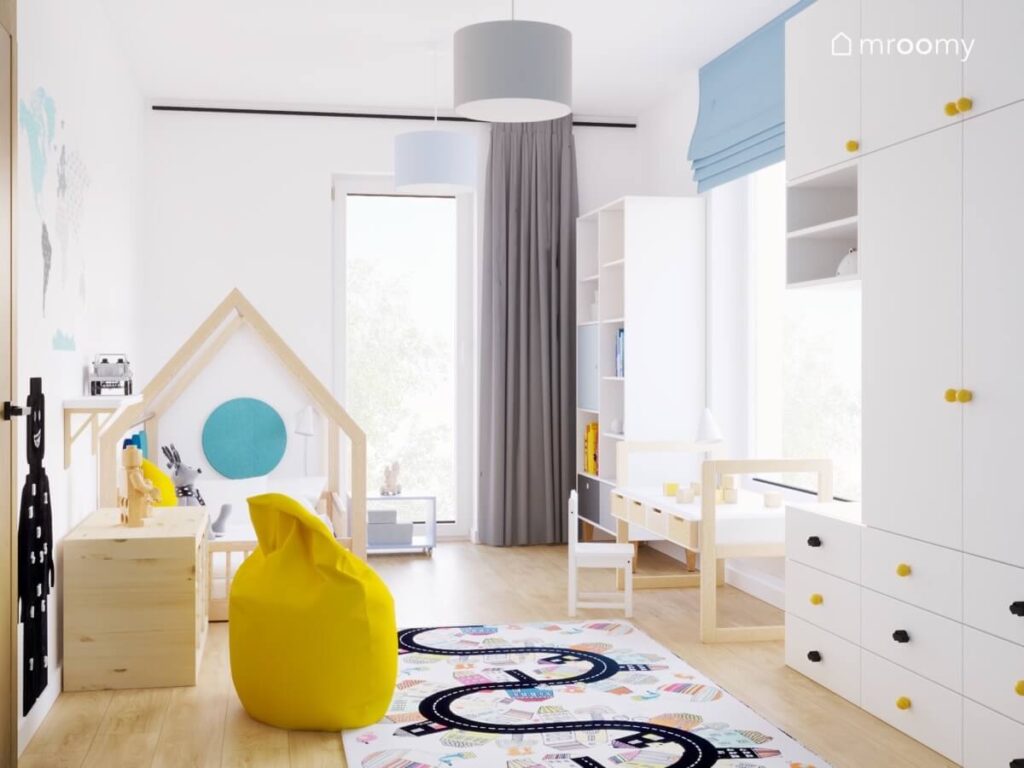 Jasny pokój dla chłopca w wieku przedszkolnym a w nim białe meble drewniane łóżko domek żółta pufa oraz dywanem przedstawiający drogę przez miasto