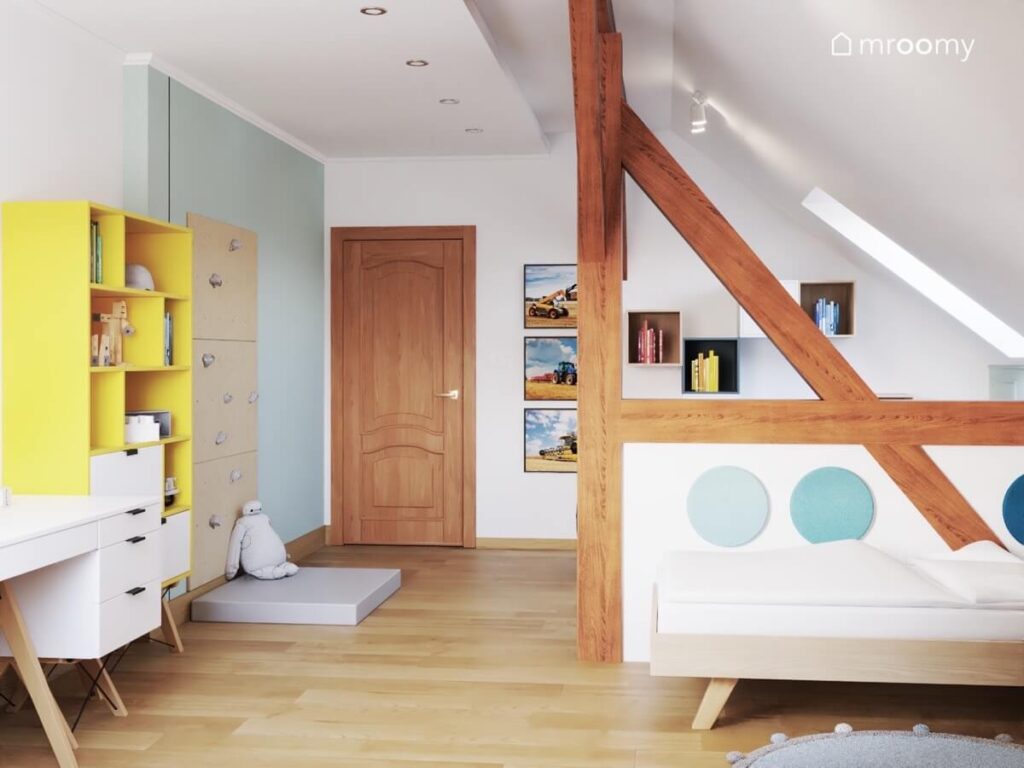 Jasny pokój na poddaszu dla chłopca a w nim drewniane łóżko uzupełnione niebieskimi panelami żółty regał i drabinka gimnastyczna