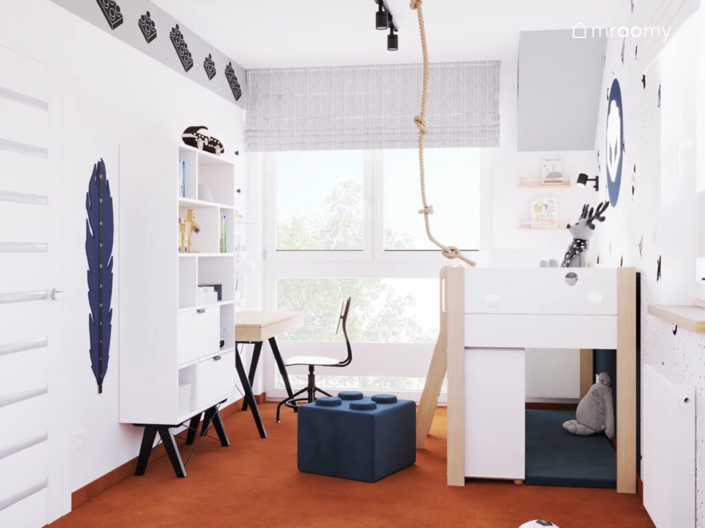 Biały pokój dla sześcioletniego chłopca a w nim szary pasek z klockami pod sufitem białe i drewniane meble oraz pufka w kształcie klocka