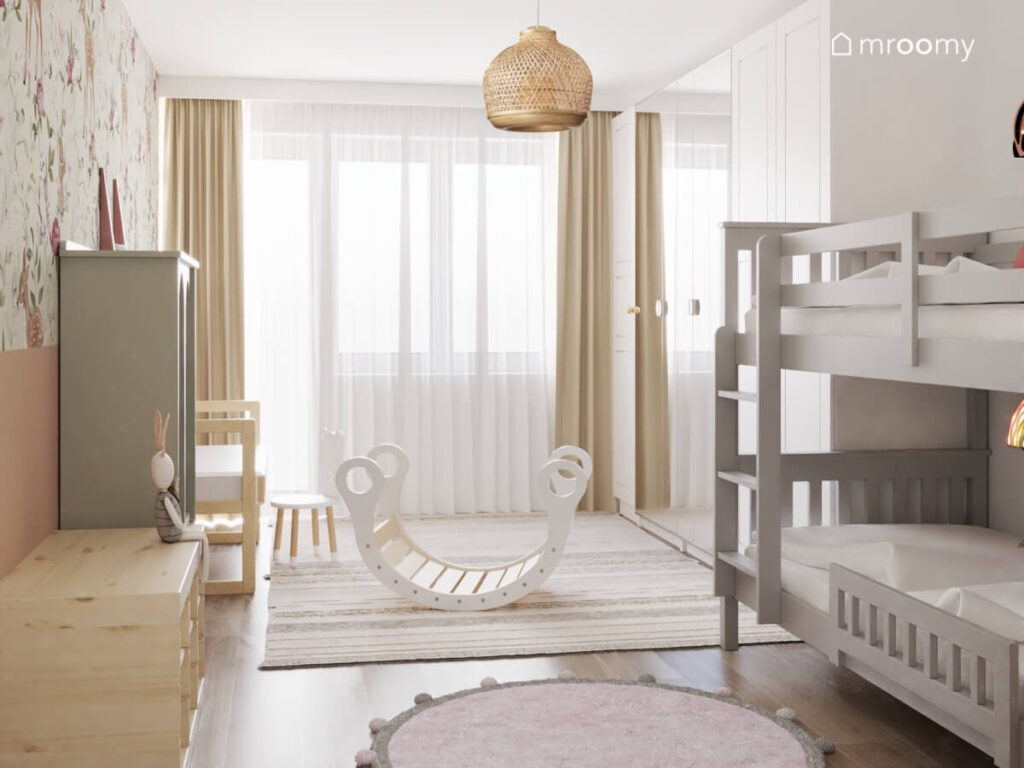 Szare łóżko piętrowe uzupełnione różowymi panelami ściennymi i uroczymi lampkami nocnymi z drewna a obok wysoka biała szafa w pokoju dwóch małych dziewczynek