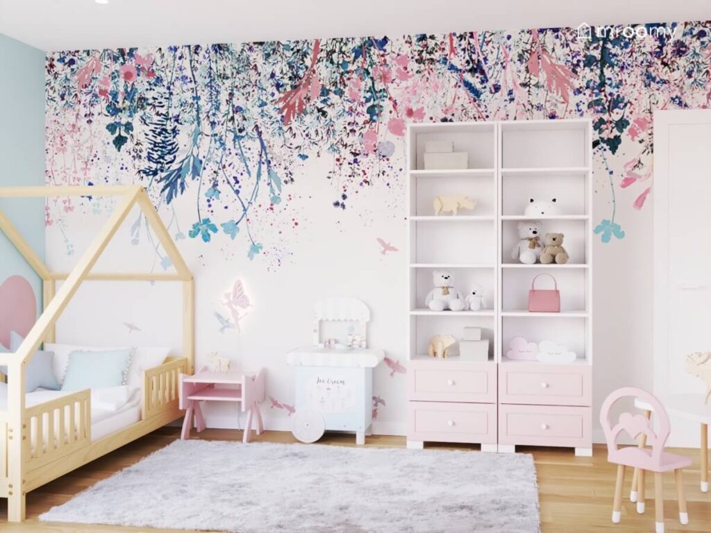 Ściana pokryta tapetą w kwiaty a na niej drewniane łóżko domek i dwa duże regały w pokoju czterolatki