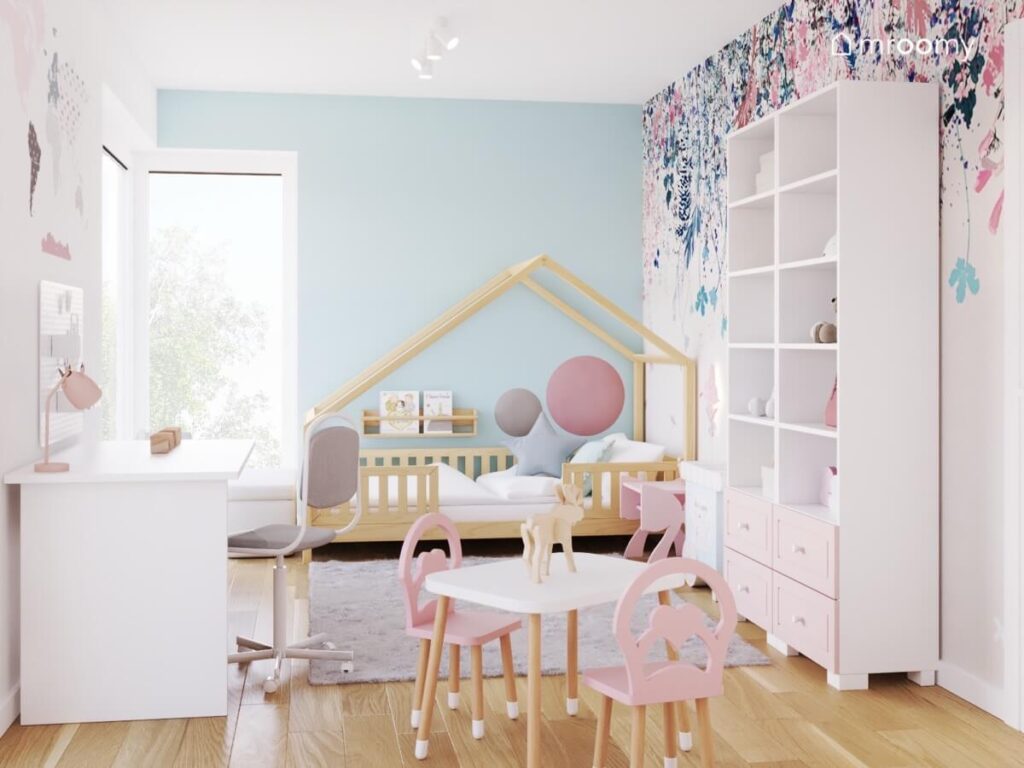 Biało niebieski pokój dla dziewczynki z drewnianym łóżkiem domkiem białymi regałami oraz stolikiem z krzesełkami z ozdobnymi oparciami