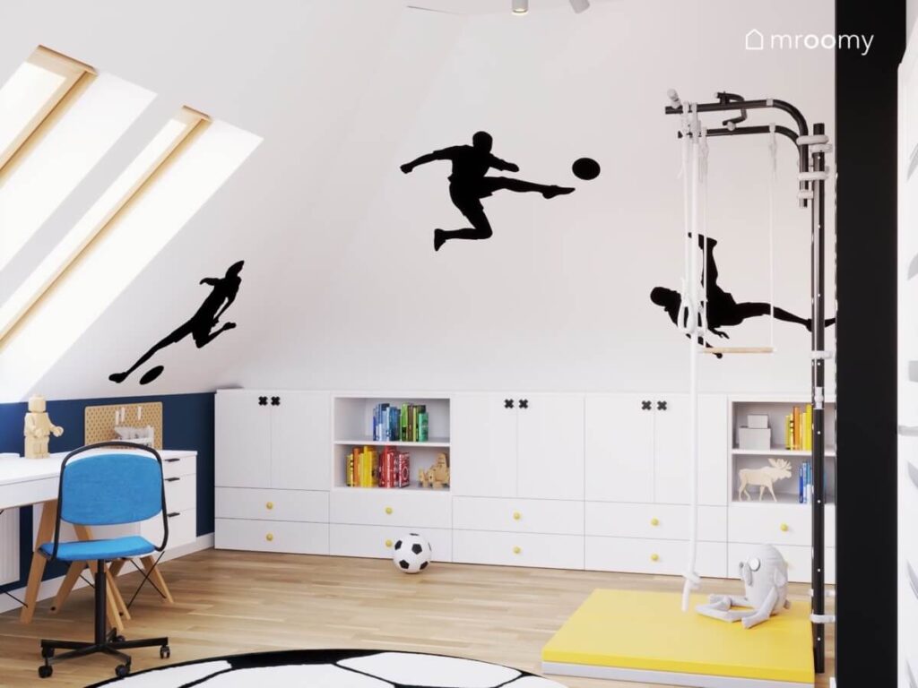 Białe ściany z naklejkami w kształcie piłkarzy a pod nimi niskie białe szafki w pokoju dla chłopca w wieku szkolnym